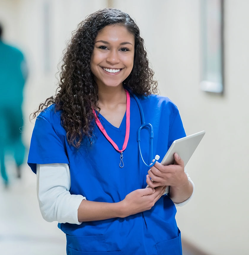 Young nurse in hospital hallway holding digital tablet patient chart