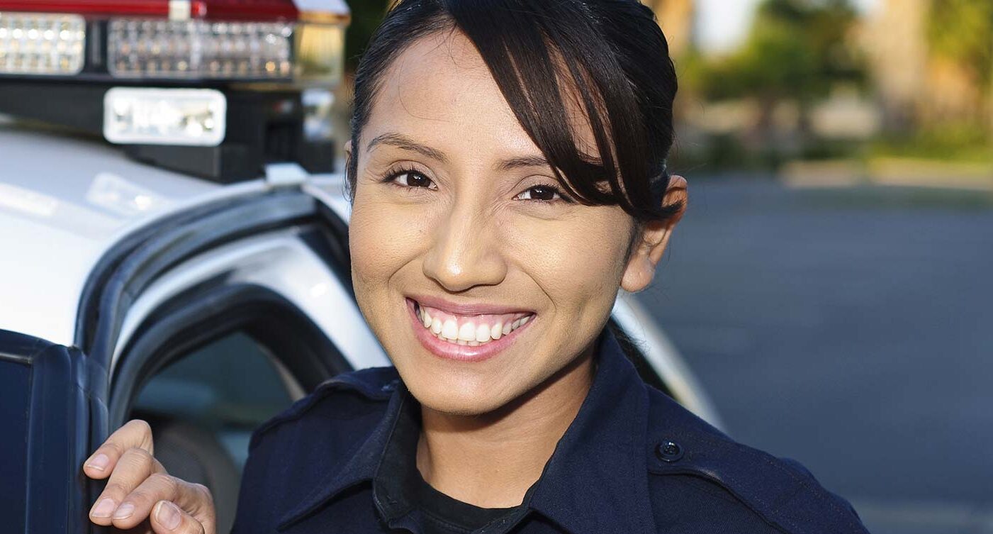 a Hispanic police officer smiling next to her unit.