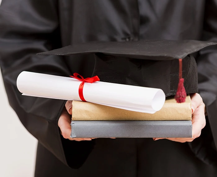Graduate holding diploma and books in cap and gown at Platt College.