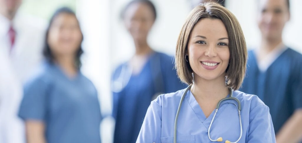 Smiling female nurse with stethoscope and colleagues in medical uniforms.