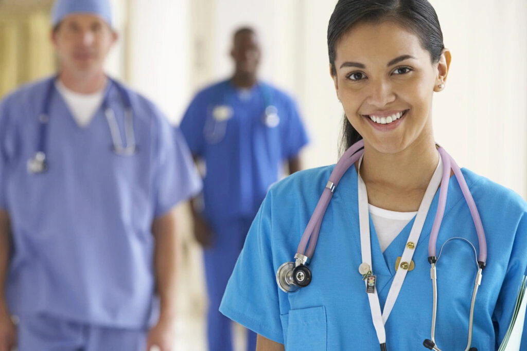 Smiling female nursing student with stethoscope in clinical setting.