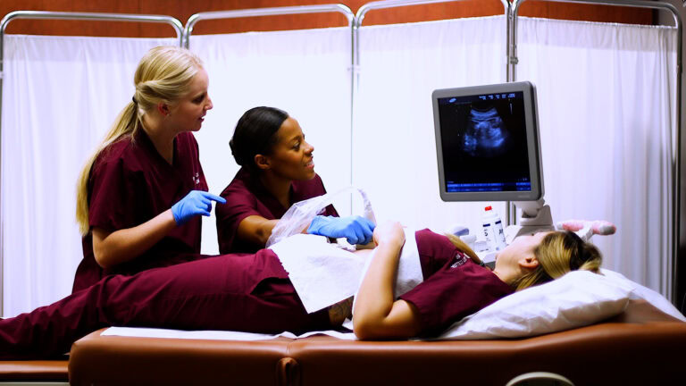 Medical students practicing ultrasound techniques on a patient in a clinical training setting.