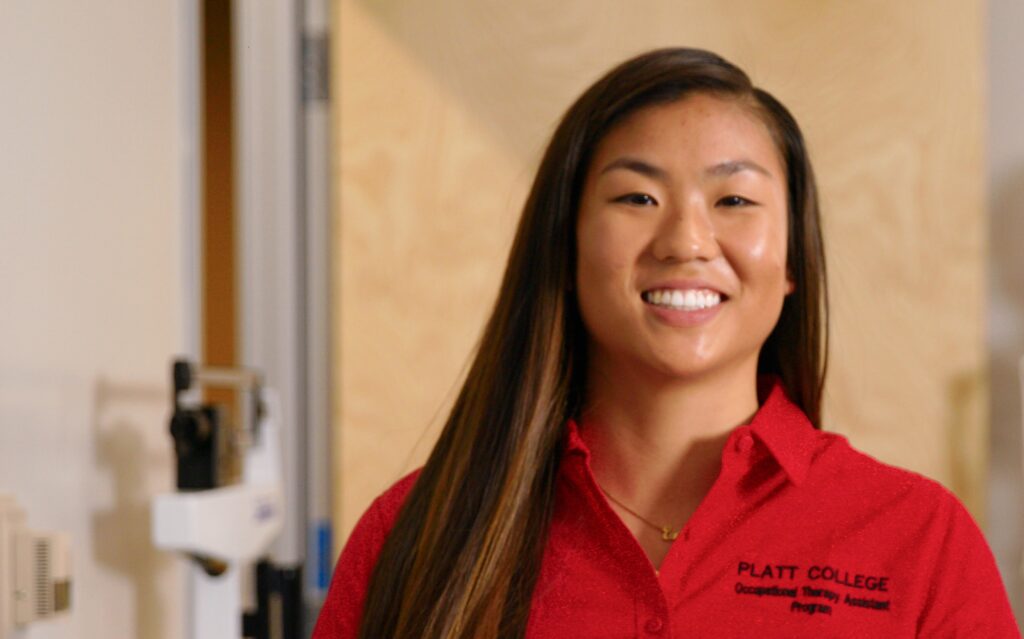 Smiling female student in red Platt College uniform in classroom setting.